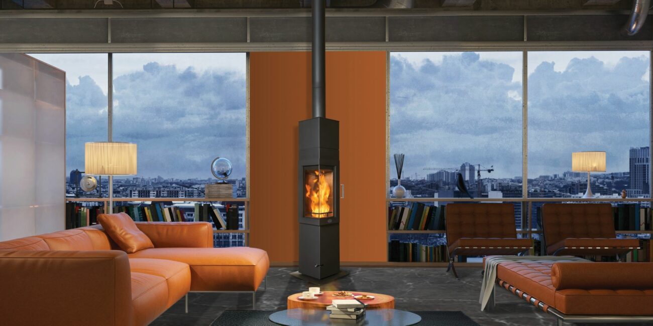 Tall dark stove burning in a living room with orange sofas and large windows overlooking the city