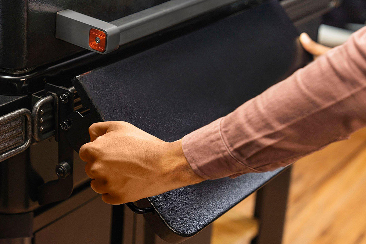 Person folding the black front shelf on a Traeger grill