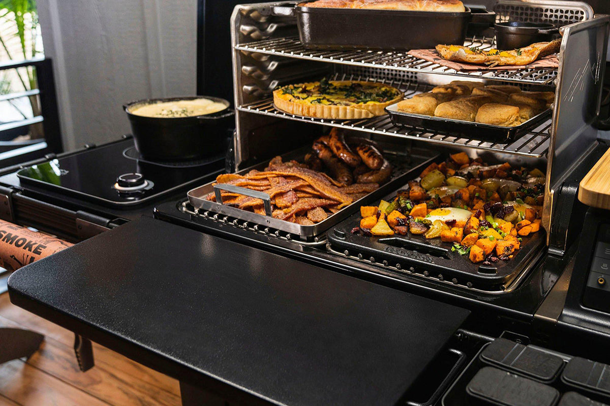 Traeger grill with its front shelf extended beneath racks filled with food