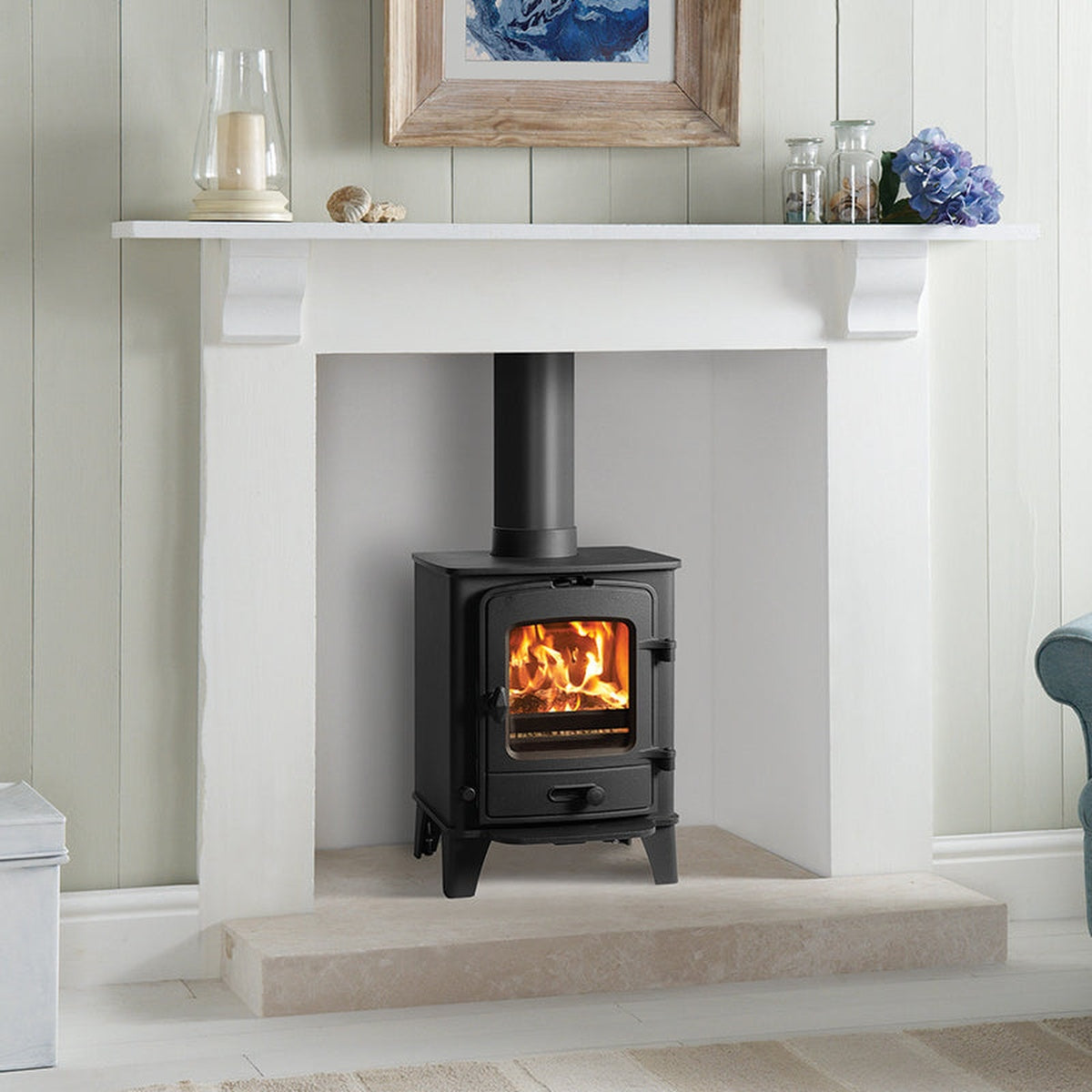 Stovax County 3 stove in a white fireplace beside a blue armchair