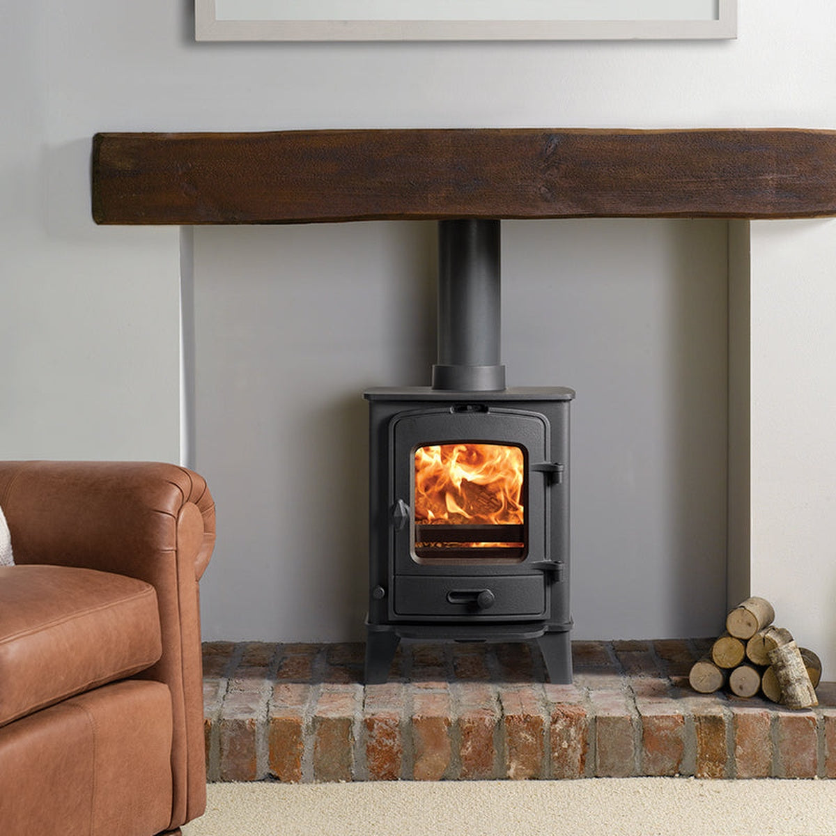 Stovax County 3 stove beneath a timber beam beside a brown armchair
