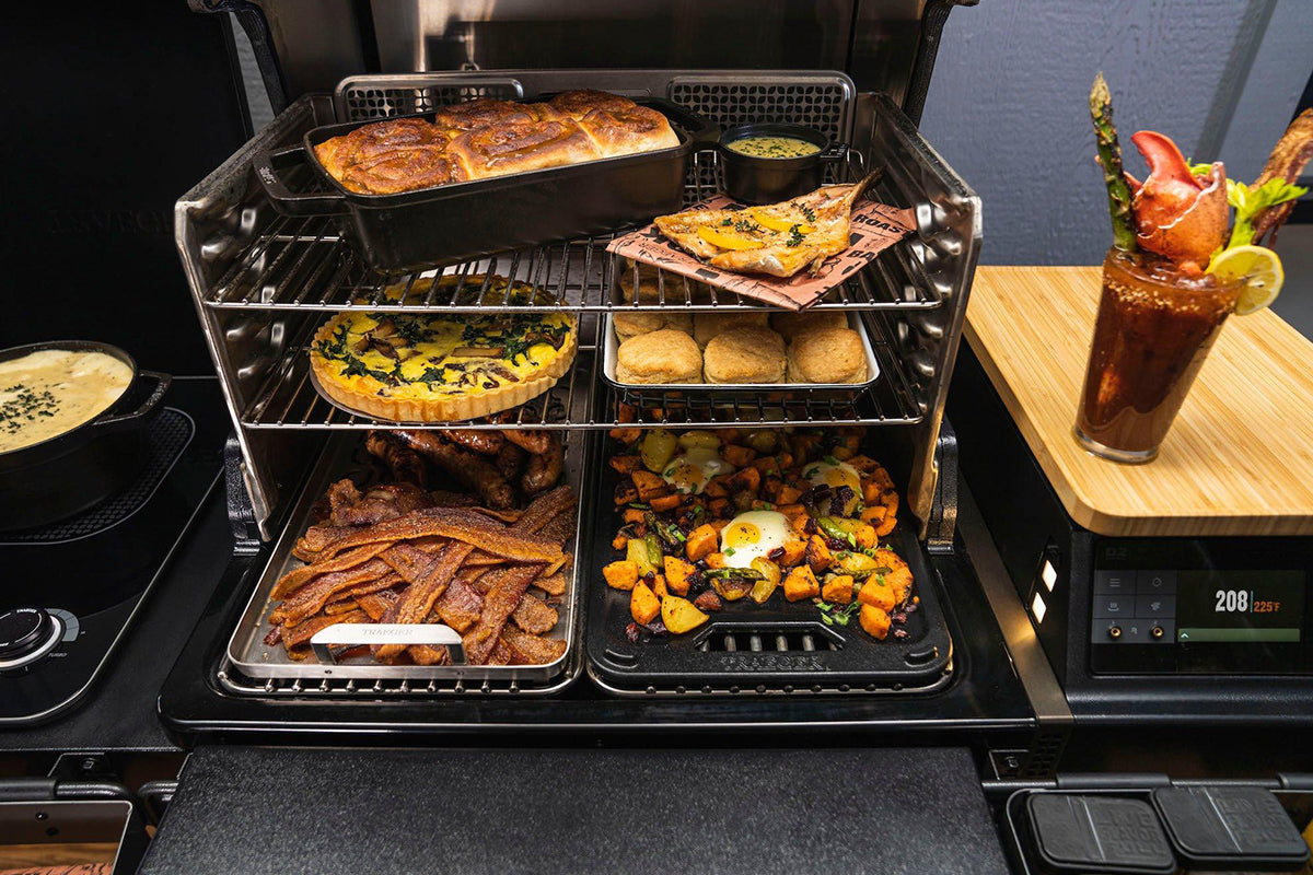 Open Traeger grill filled with breakfast dishes, with the cast iron griddle on the lower rack