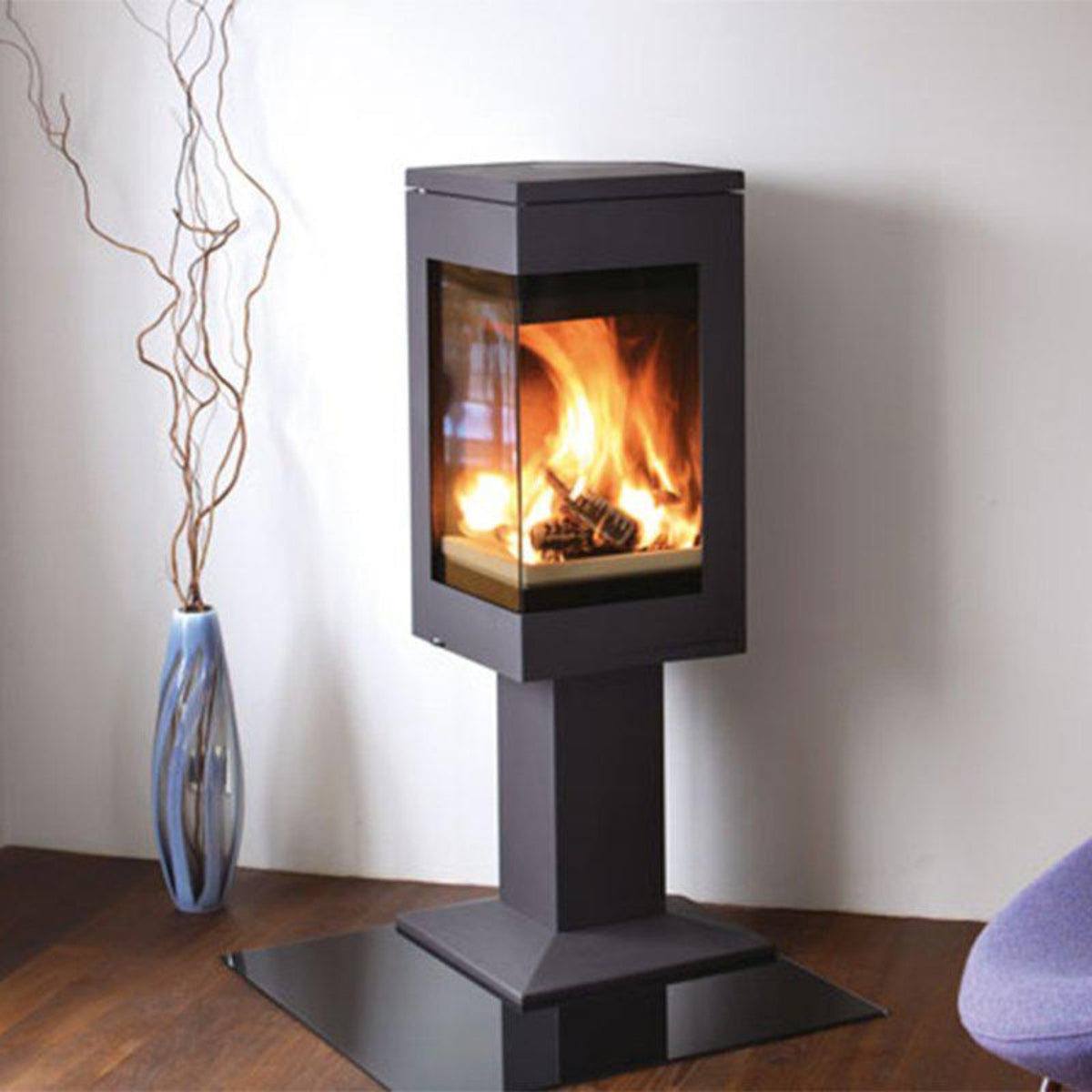 Nordpeis Quadro 1 pedestal wood stove beside a purple chair