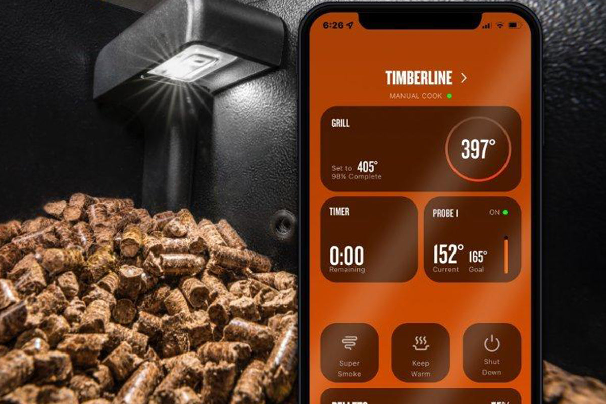 Traeger pellet sensor above wood pellets beside a phone displaying the Traeger app
