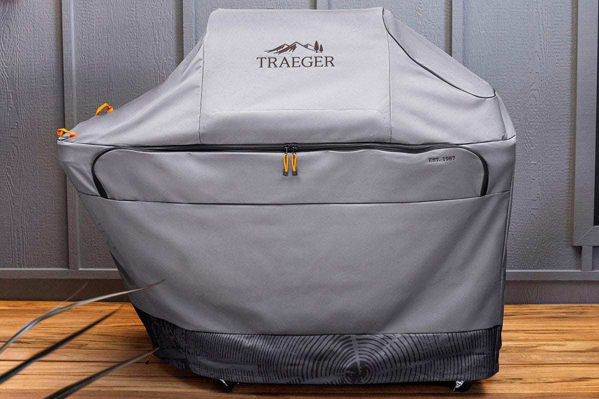 Traeger Timberline grill under its grey cover on a wooden deck beside a grey wall