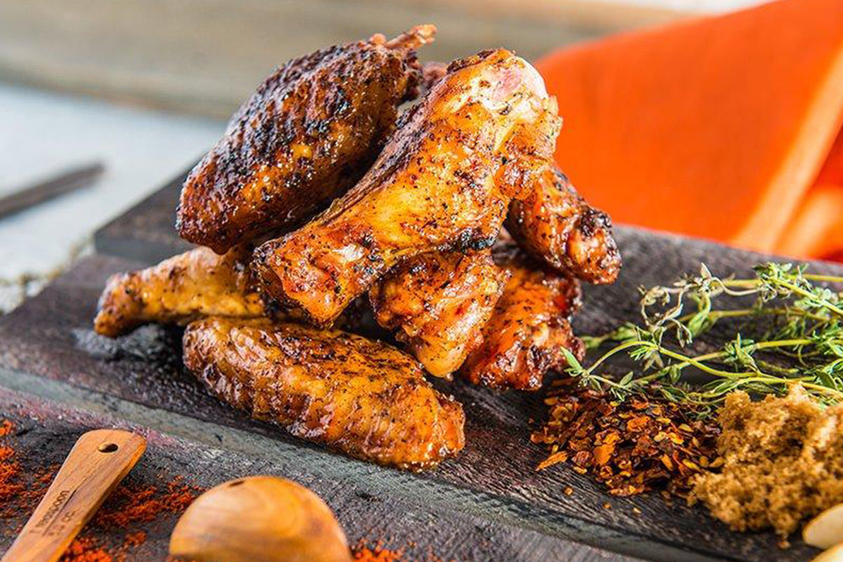 Juicy grilled chicken coated with Traeger Rub, displayed on a rustic wooden board alongside scattered spices, fresh herbs, and a wooden spoon. The chicken's crispy exterior showcases the Traeger Rub's rich seasoning.