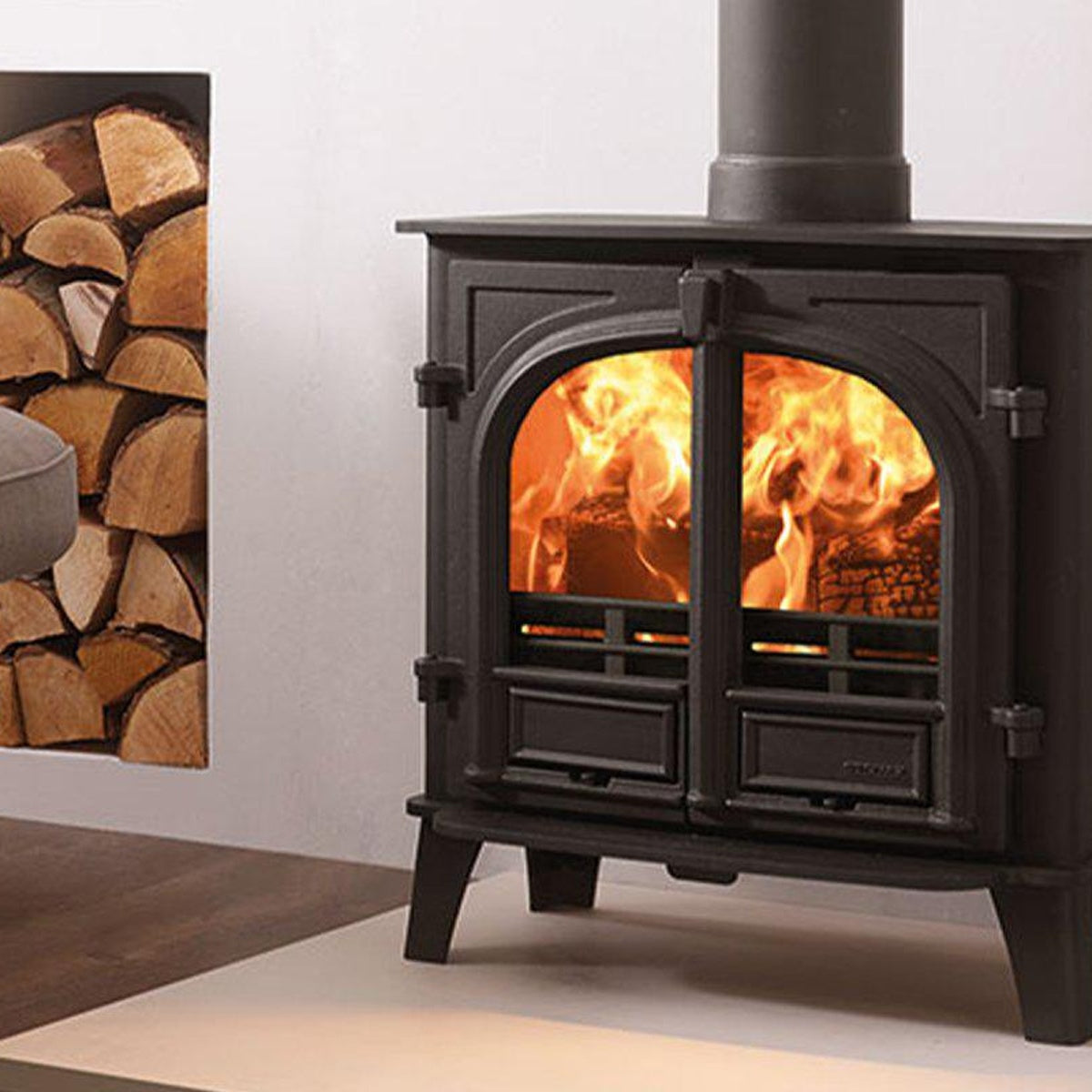 Stovax Stockton 5 Wide Matt Black double-door fixed-grate multi-fuel stove beside a log stack