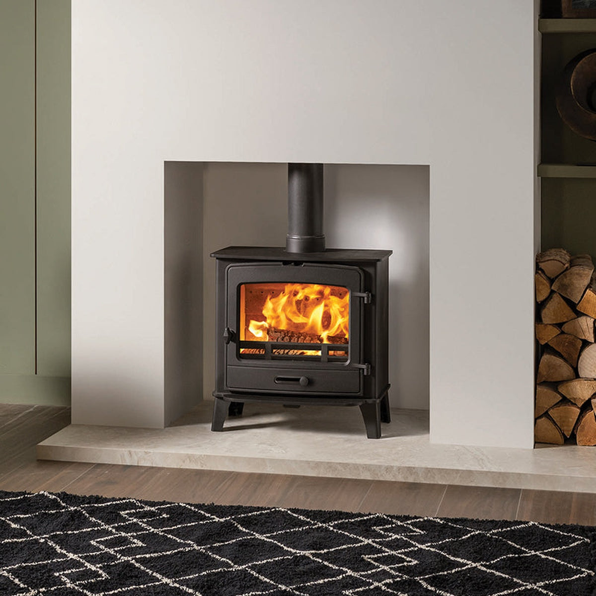 Stovax County 5 Wide stove in a white recess beside a log store