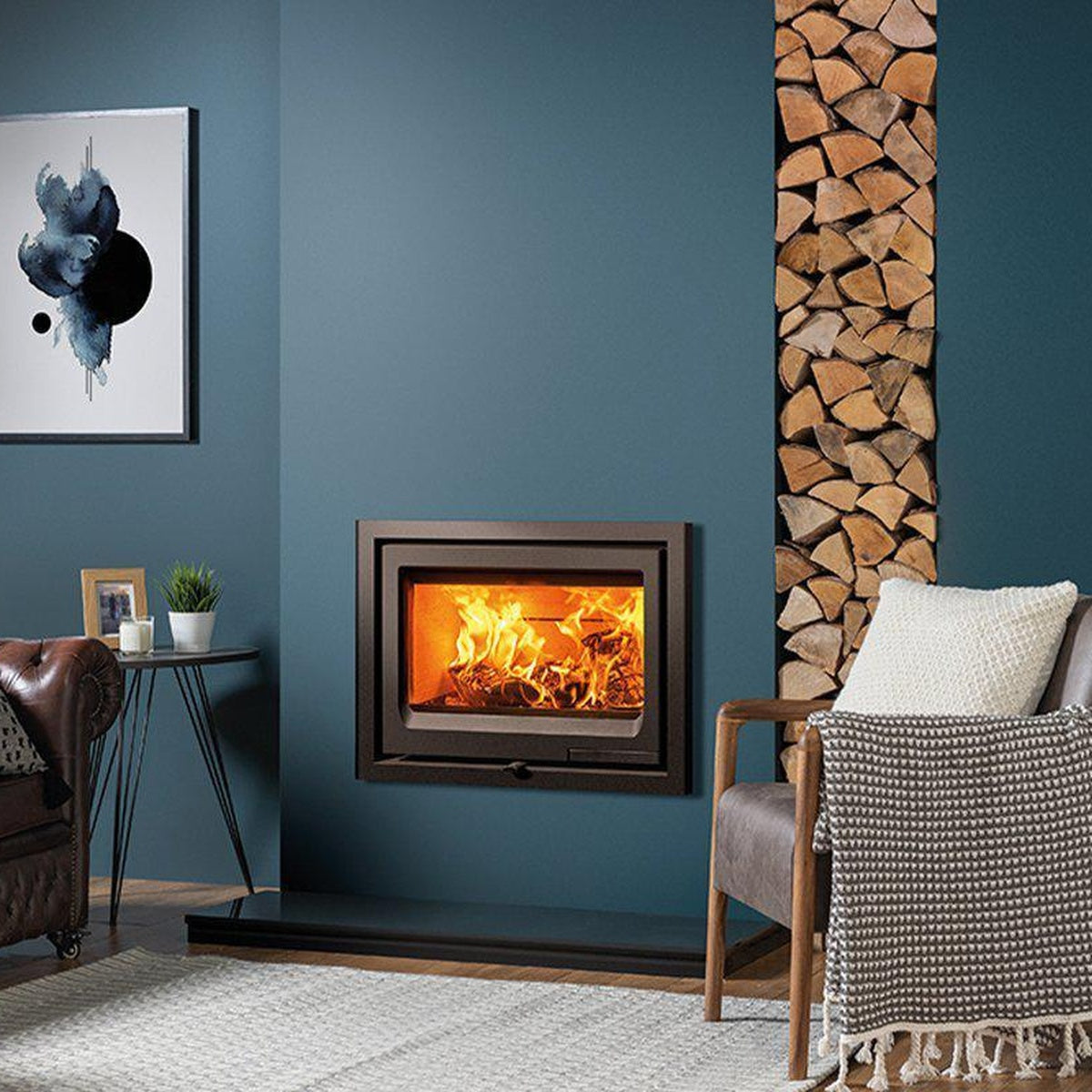 Stovax Vogue 700 Inset wood fire against a blue wall beside stacked logs