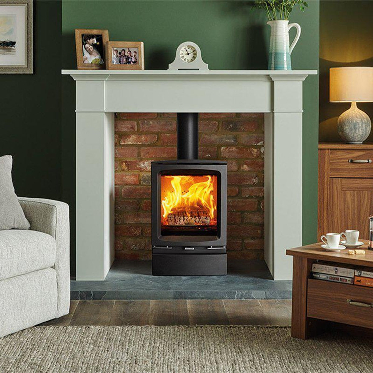 Stovax Vogue Midi stove with plinth in a brick fireplace against a green wall
