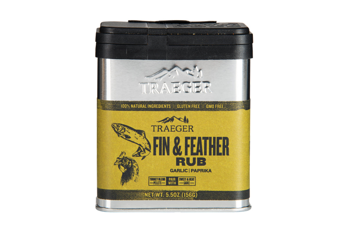 Close-up of the Traeger Fin & Feather Rub aluminium tin. Vibrant yellow label displays illustrations of a fish and a bird, with text highlighting "100% Natural Ingredients, Gluten Free, GMO Free." The tin also mentions key flavours "Garlic | Paprika" and suggests pairing with "Turkey Blend Pellets" and "Sweet & Heat BBQ Sauce".