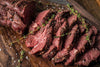 Sliced tender steak seasoned with Traeger beef rub and fresh rosemary sprigs on a wooden background.