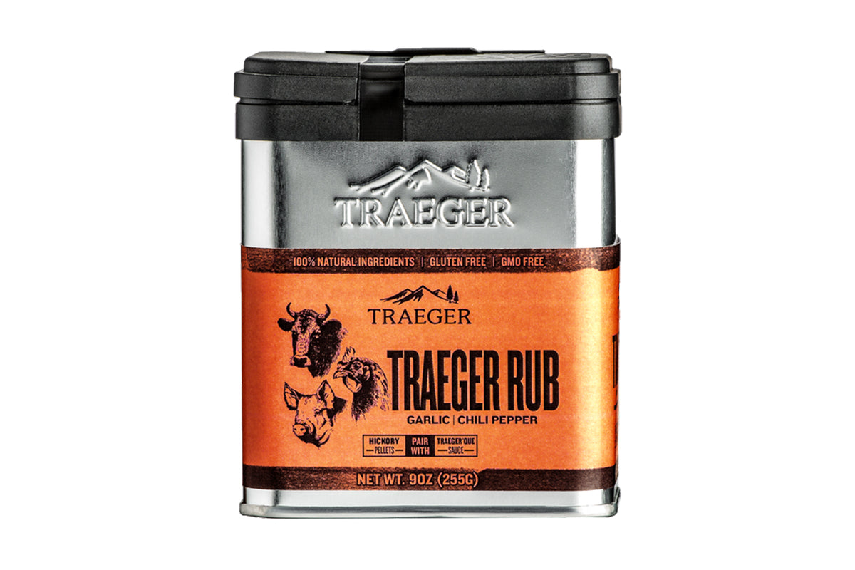 A container of "Traeger Rub" seasoning with the flavors of garlic and chili pepper. It emphasizes its 100% natural ingredients, being gluten-free, and GMO-free. The label suggests pairing with Traeger 'Que sauce. The illustration on the container depicts a cow, a chicken, and a pig.