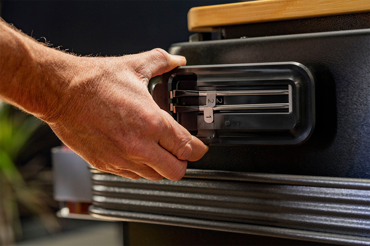 Hand holding the Traeger x MEATER probe holder against the side of a grill