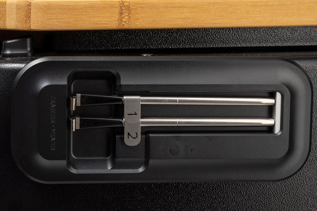 Two Traeger x MEATER probes stored in their holder on the side of a grill