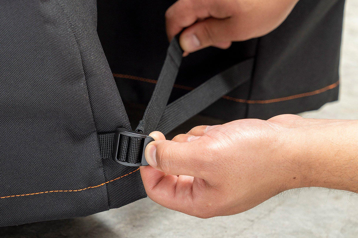Hands tightening the buckle strap at the base of the Traeger grill cover