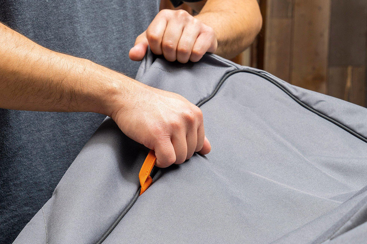 Person lifting the grey Traeger grill cover using its orange pull loop